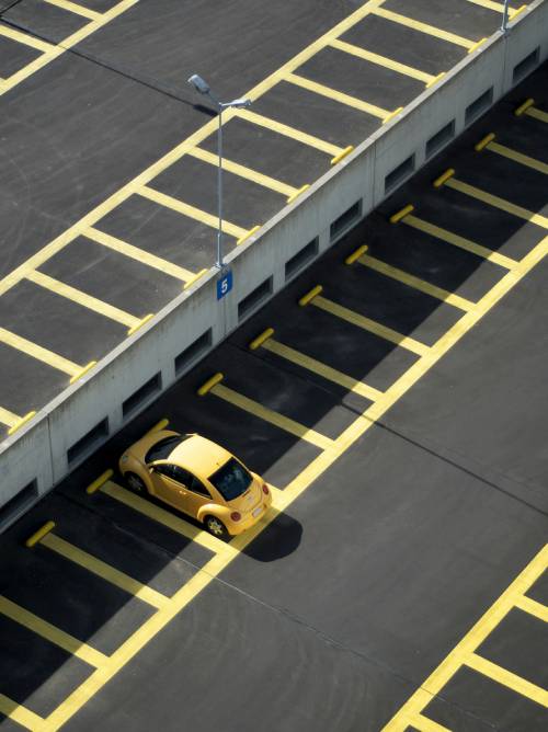 A bright yellow car parked neatly in a parking lot, surrounded by clear car park markings.