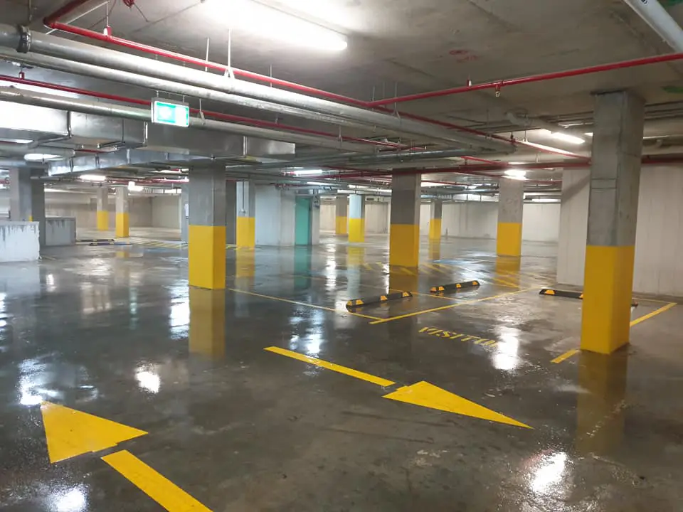 A wet parking garage featuring yellow directional arrows on a freshly sealed concrete floor.