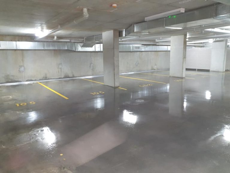 A parking garage featuring a glossy floor with yellow lines, showcasing the effects of concrete sealing.