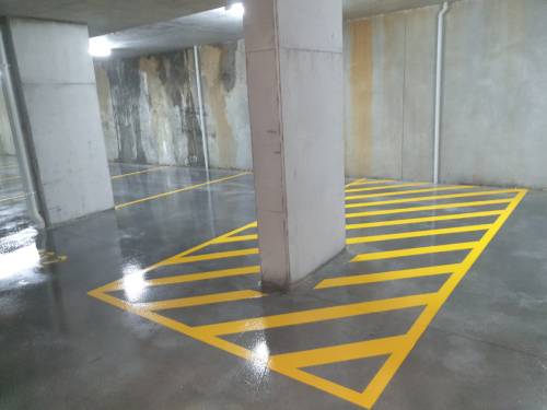 A parking garage floor featuring yellow lines on a sealed concrete surface.